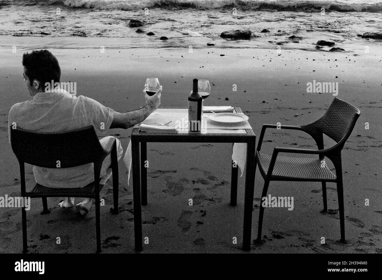 Young man dressed in white waiting for celebrating a romantic dinner on the beach. Stock Photo