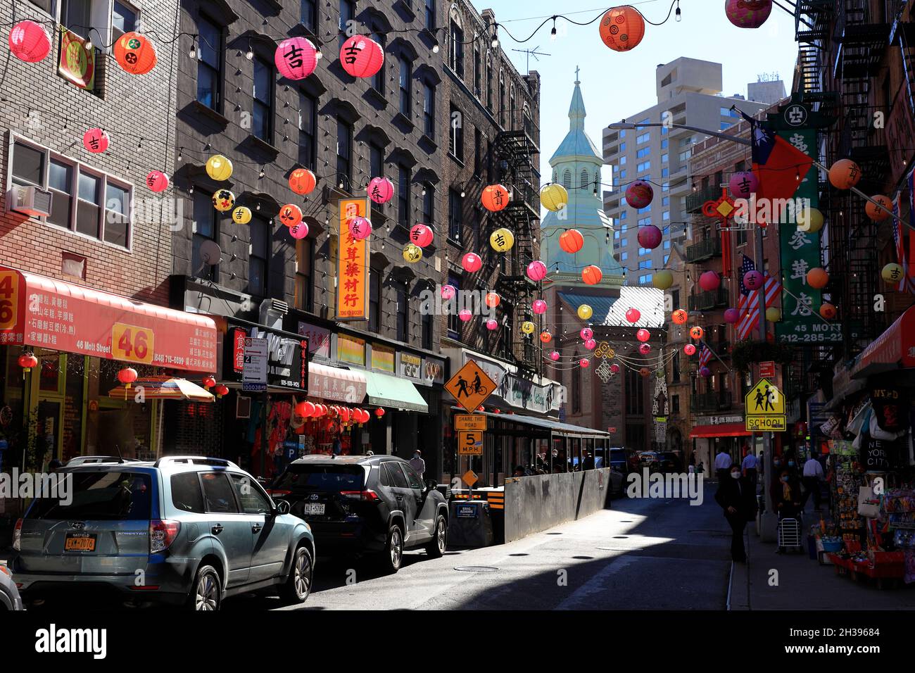 Mott Street in Chinatown with traditional style lanterns hanging over the street and the tower of the Transfiguration Church in the background.Manhattan.New York City.USA Stock Photo