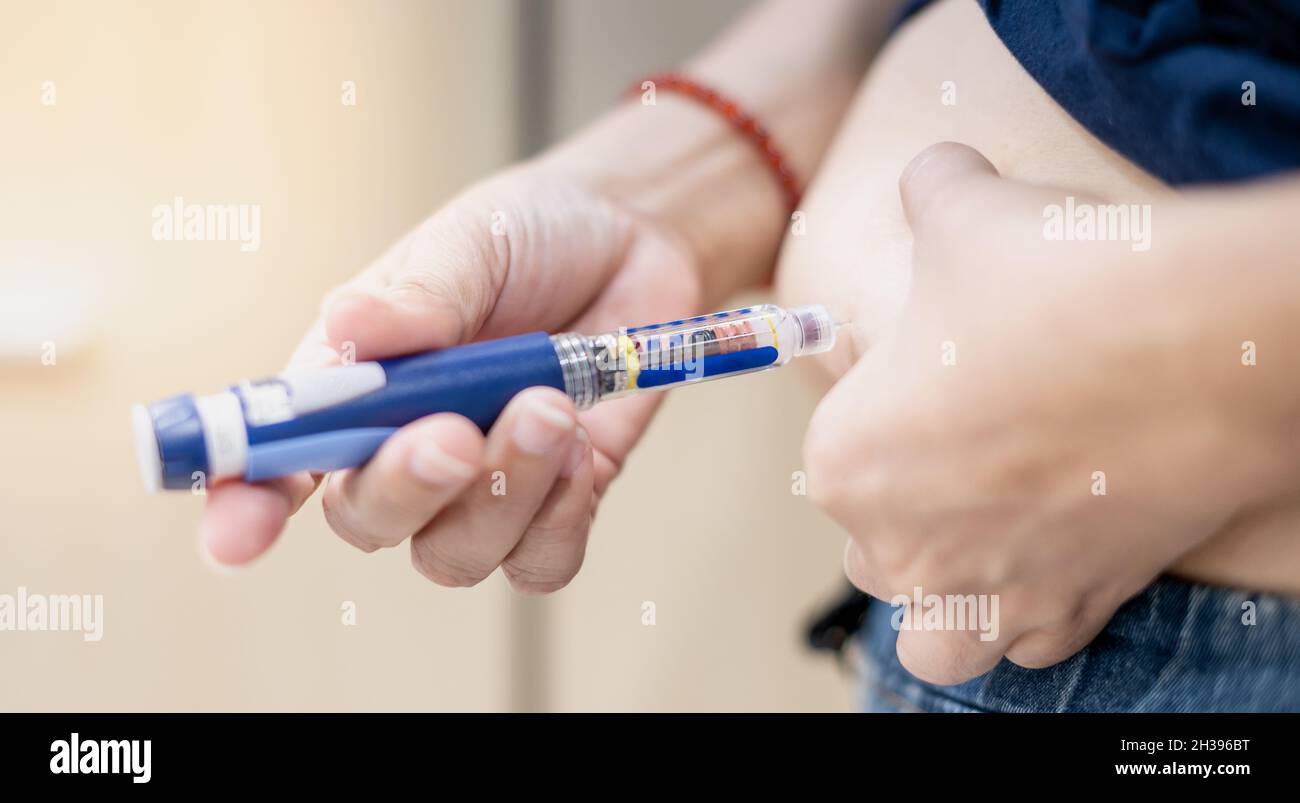 The diabetic patient hand using the insulin pen injection medical equipment to check and control the diabetics at home. Stock Photo