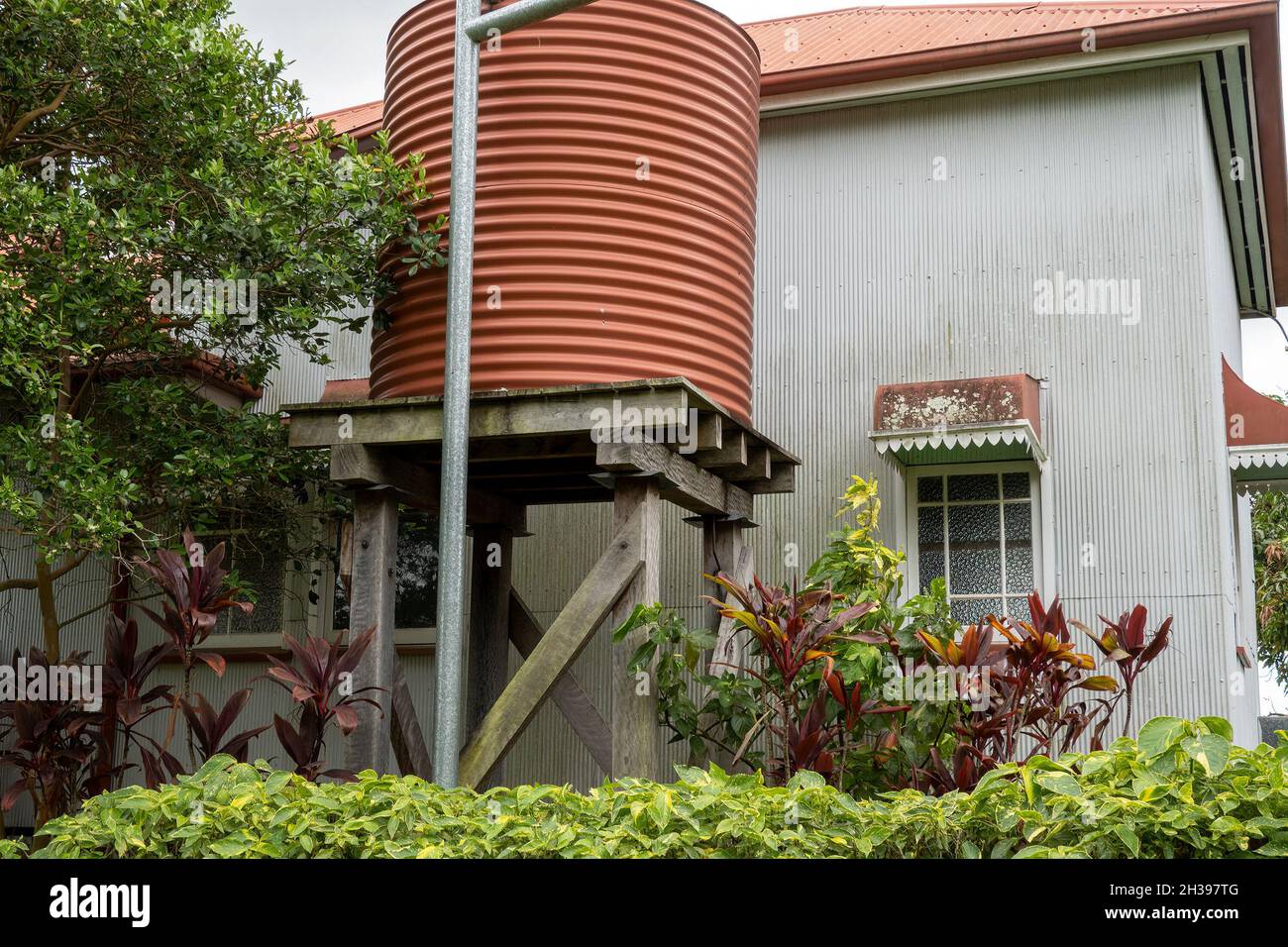 A red corrugated iron vintage tank stand on wooden posts beside the heritage listed home of a pioneering family in Australia, built in 1915 Stock Photo