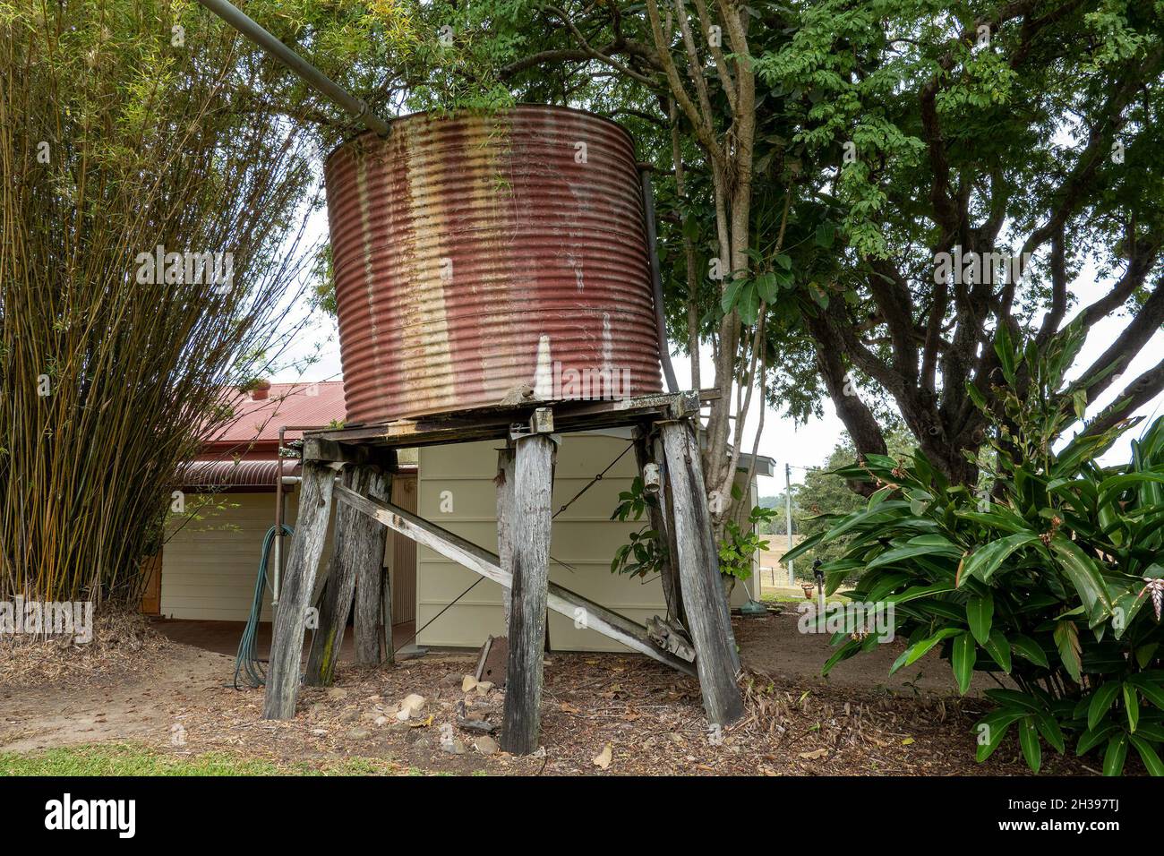 A red corrugated iron vintage tank stand on wooden posts with a distinct lean Stock Photo