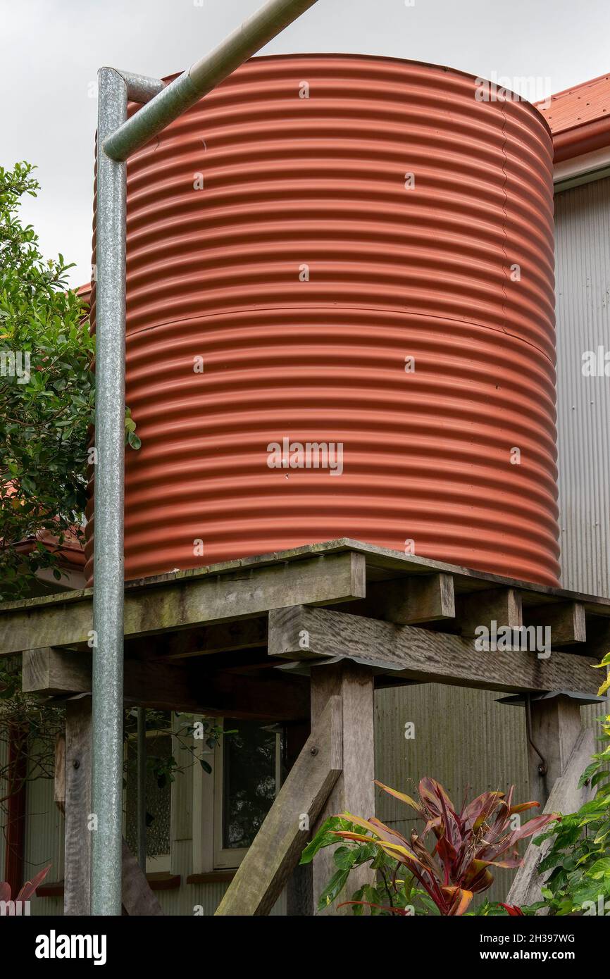 A red corrugated iron vintage tank stand on wooden posts beside the heritage listed home of a pioneering family in Australia, built in 1915 Stock Photo