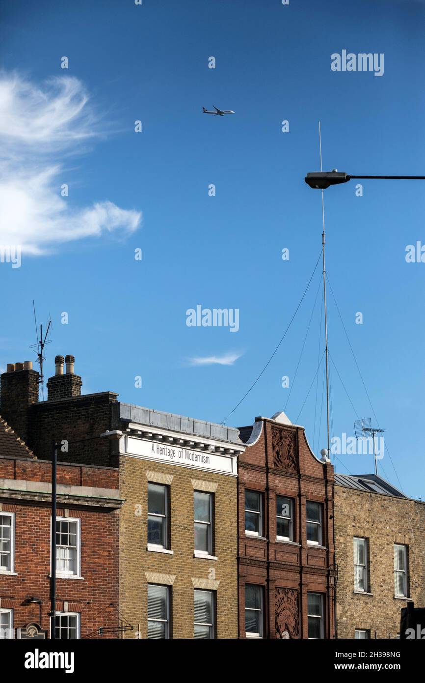 A plane flies over buildings on Commercial Street, Spitalfields, east London Stock Photo