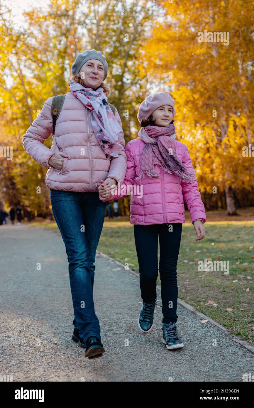 Walking in the park with children. Cute and joyful smiling caucasian mom and daughter spend time in the autumn park. Sunny fall day. A happy family. P Stock Photo