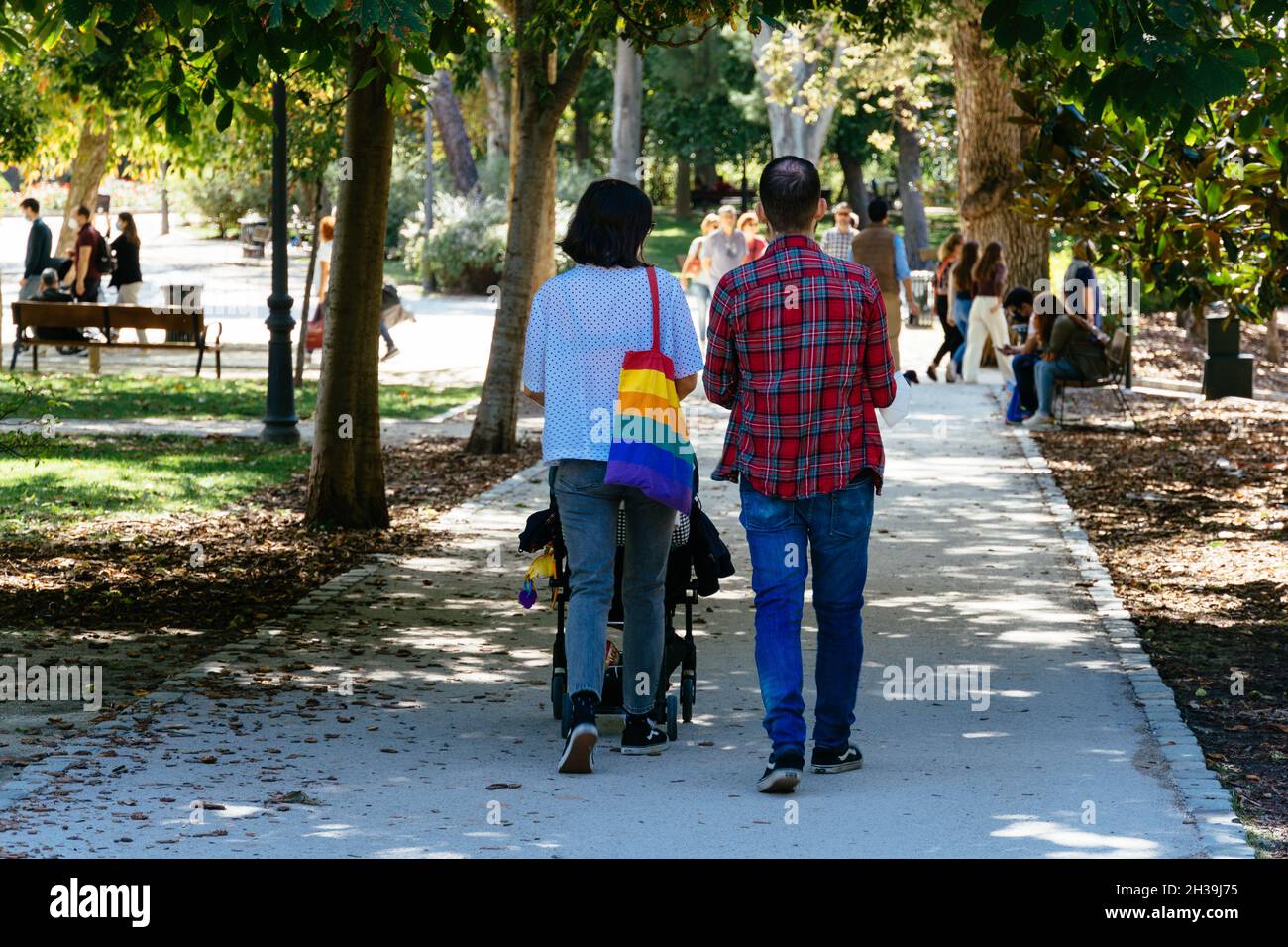 Madrid, Spain - September 26, 2021: Young couple walking with a baby stroller in the retiro park in Madrid. She carries a bag with gay pride colors. Stock Photo