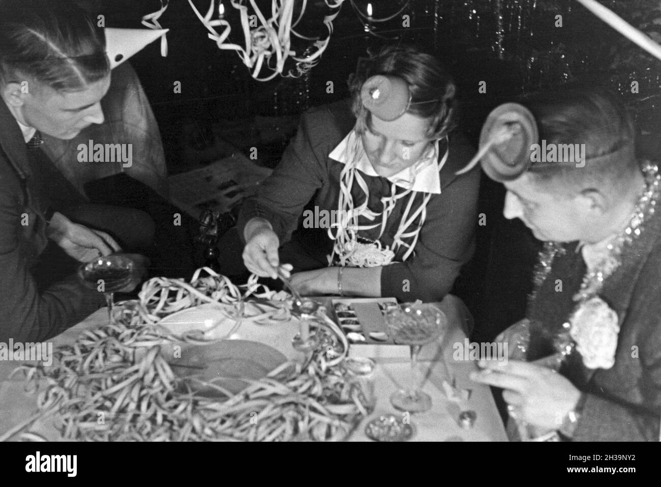 Zwei Männer und eine Frau beim Bleigießen auf einer Silversterfeier, Deutschland 1930er Jahre. Two men and a woman doing molybdomancy at a New Year's Eve party, Germany 1930s. Stock Photo