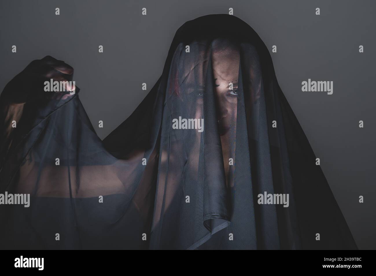 Redhead woman with a black veil on her head in a dark studio. A girl ...