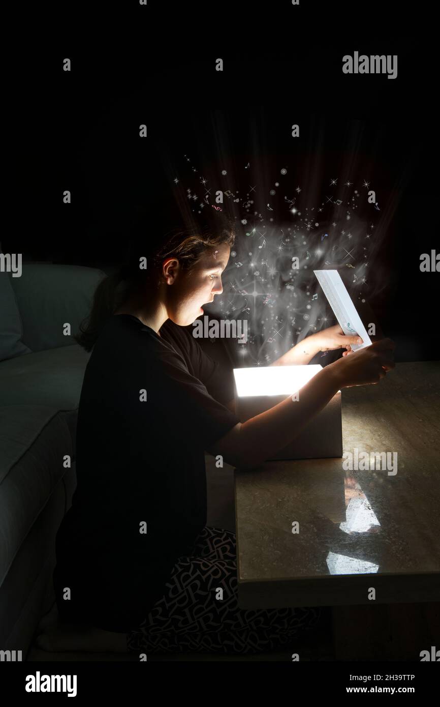 Young girl pre teen 11 12 13 opening a surprise magical glowing gift box with light glitter smoke and music Stock Photo