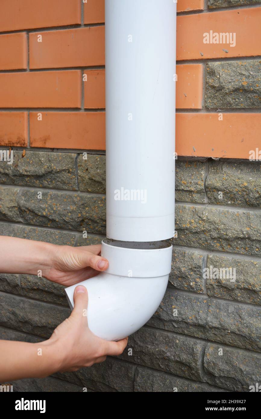 Worker Installing rain gutter downspout pipe. Contractor hands repair