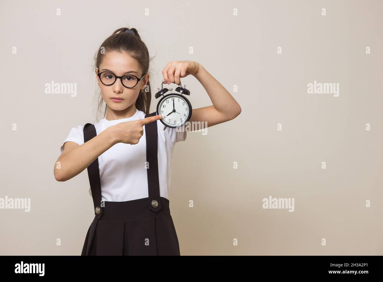 Girl holding an alarm clock. Girl shows her finger at the clock. Space for text Stock Photo