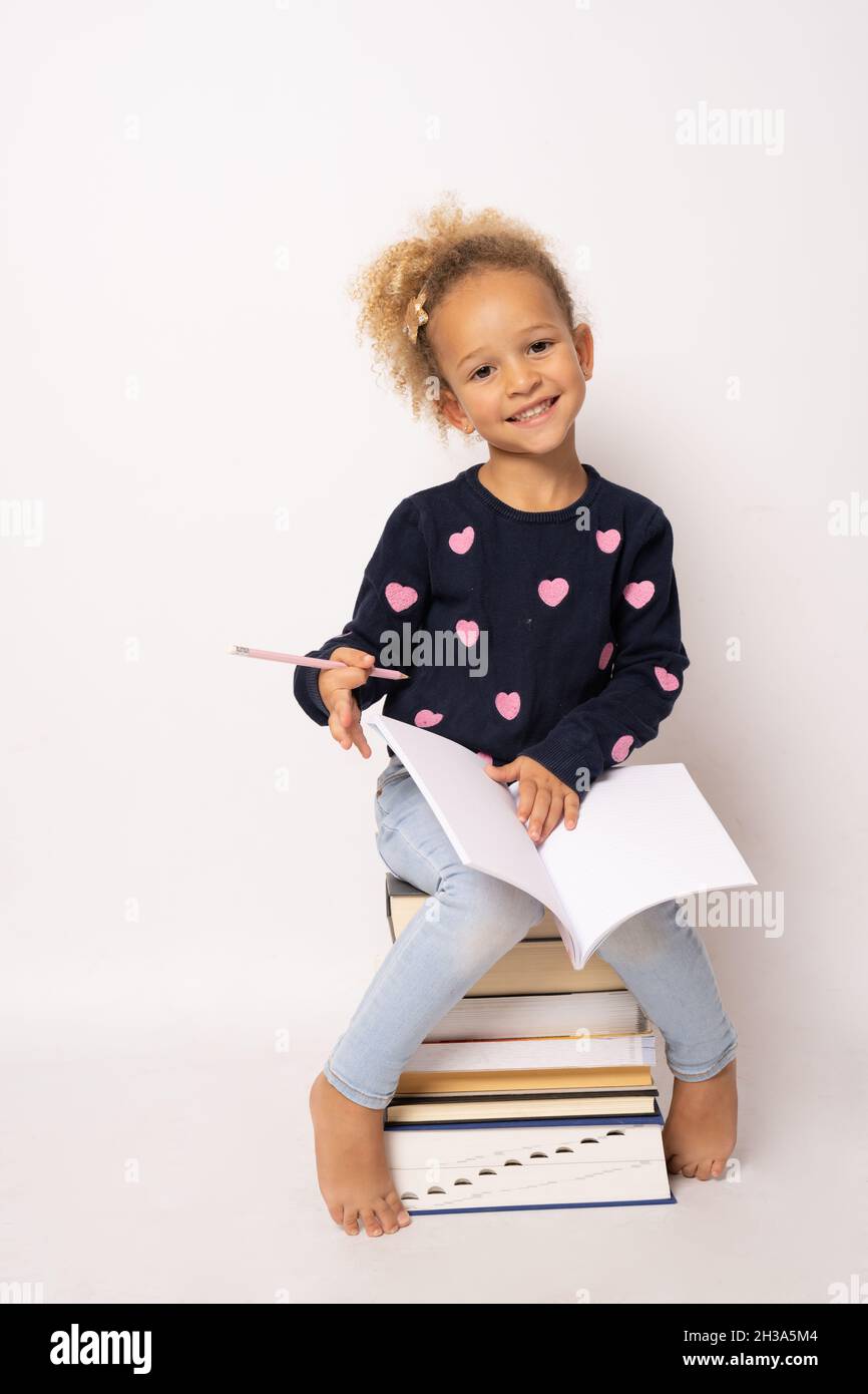 Little cute girl sitting on stack of books with a notebook. Isolated ...