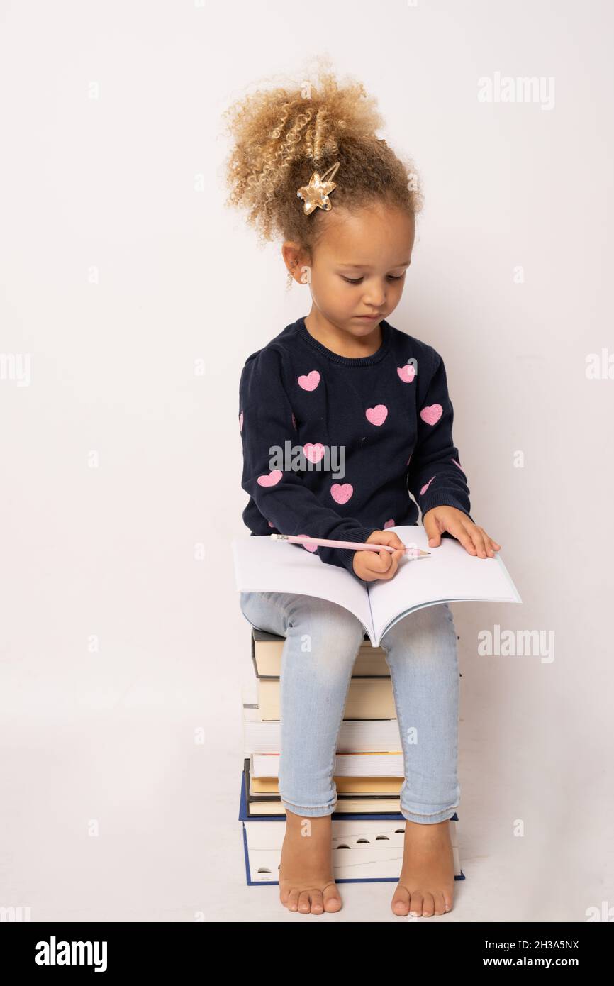 Little cute girl sitting on stack of books with a notebook. Isolated ...