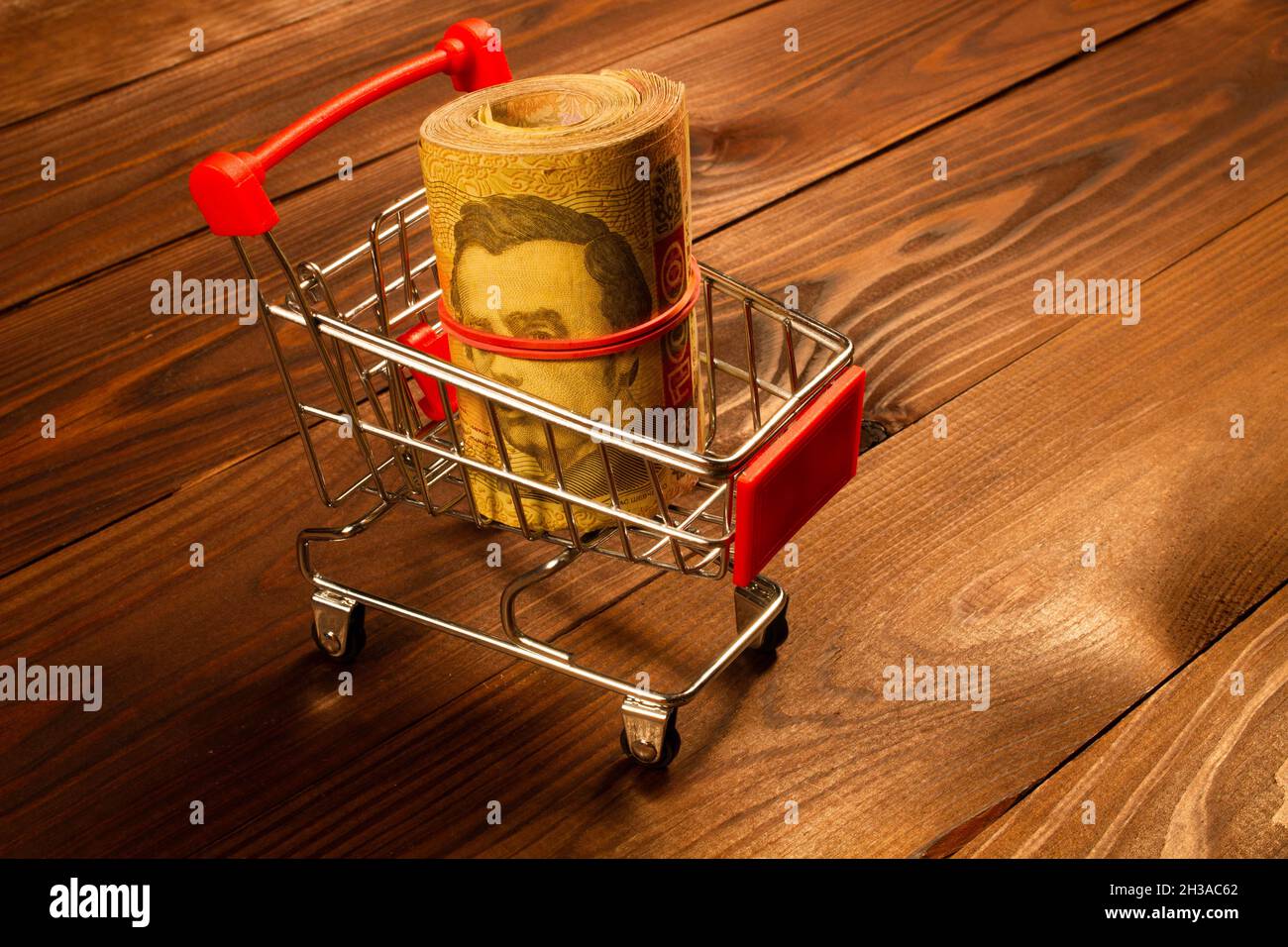 Black Friday concept. Wad of Money in the shopping cart. Ukrainian hryvnia in a small metal shopping cart on a beautiful wooden background. Ready to s Stock Photo