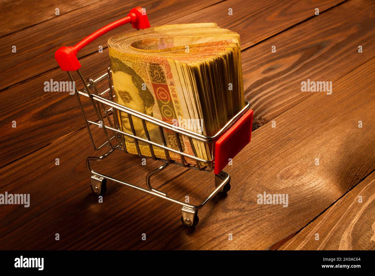 Black Friday concept. Wad of Money in the shopping cart. Ukrainian hryvnia in a small metal shopping cart on a beautiful wooden background. Ready to s Stock Photo