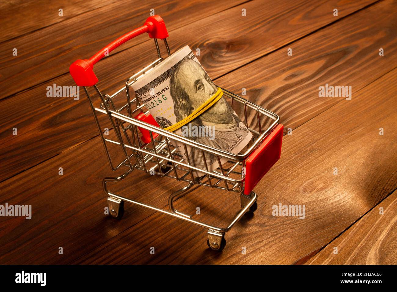 Black Friday concept. Wad of Money in the shopping cart. US dollars in a small metal shopping cart on a beautiful brown wooden background. Ready Stock Photo