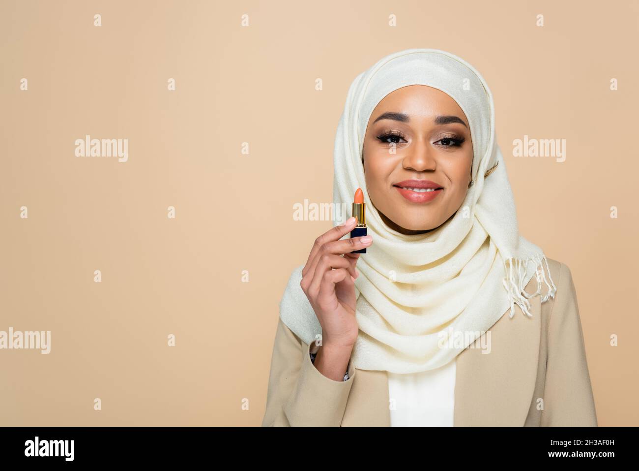 happy muslim woman in hijab holding lipstick isolated on beige Stock ...