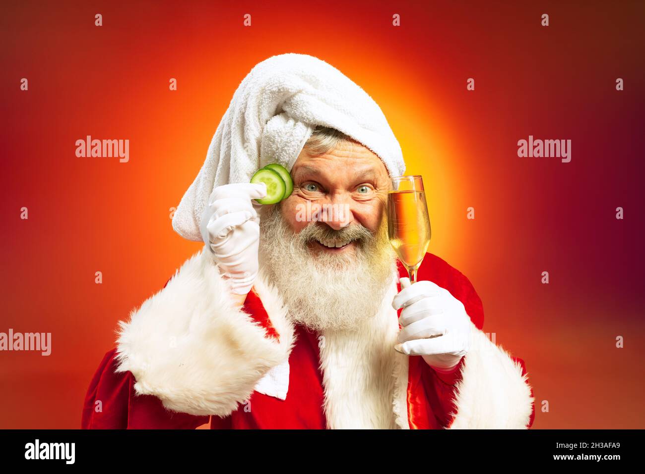 Funny senior man wearing white towl and costume of Santa Claus congrats everybody with New Year 2022 isolated on red yellow background in neon. Stock Photo