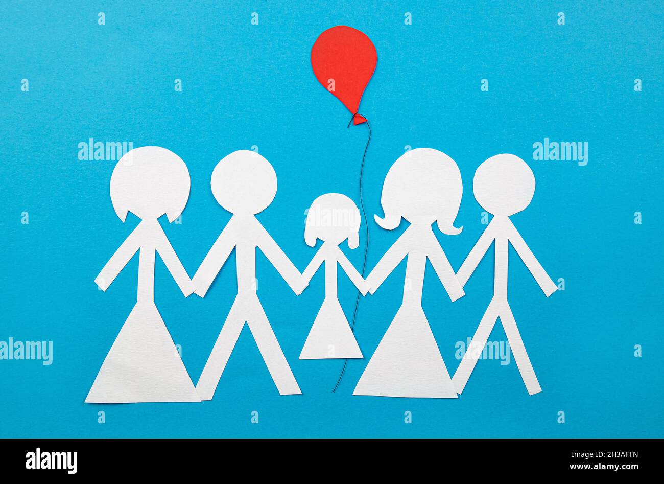 Conceptual image of co parenting. Two families sharing custody and parenting together. Two couples sharing a child with red balloon, cut out paper. Stock Photo