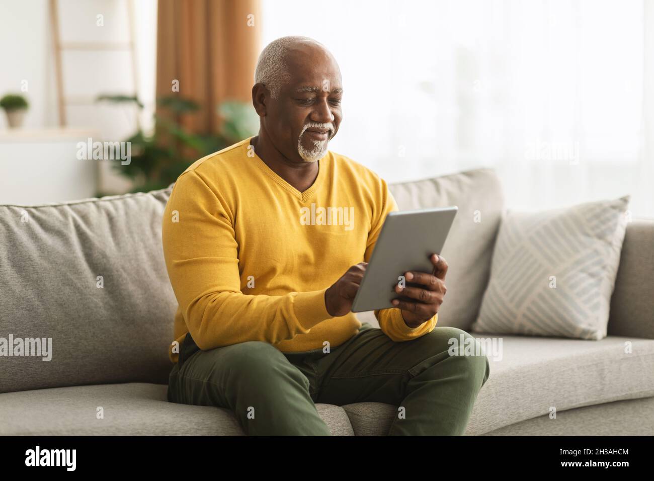 Mature African American Man Using Digital Tablet Sitting At Home Stock Photo