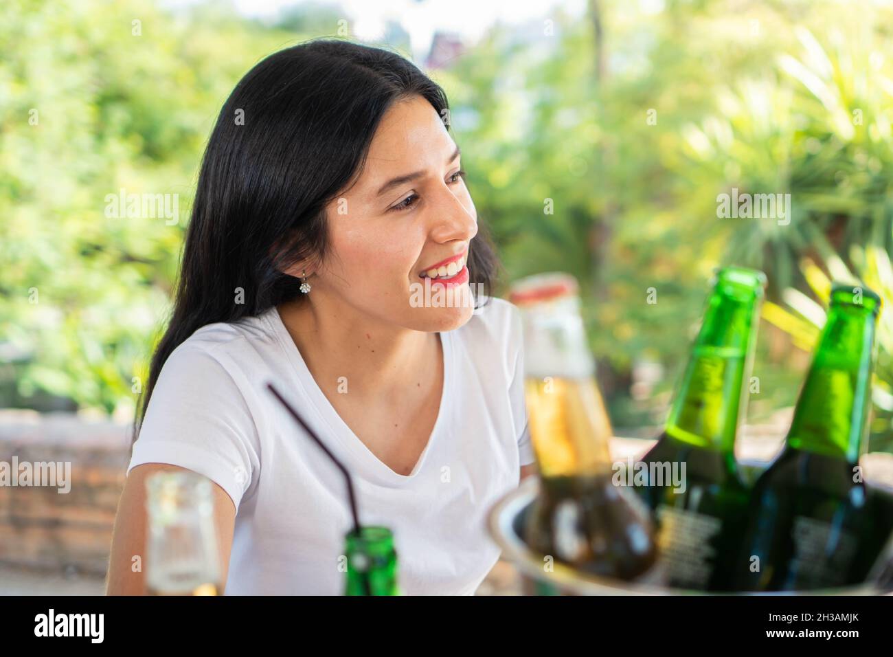 Young beautiful and smiling Latin woman in an outdoor bar with beers. Smiling brunette haired girl having a conversation with her friends in her leisu Stock Photo