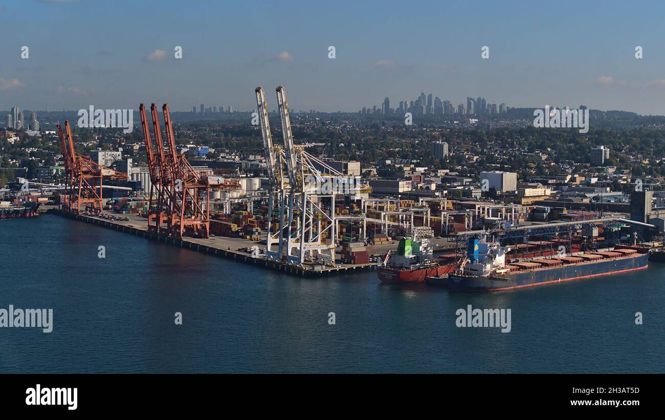 Aerial view of Vancouver container terminal with cranes and mooring bulk carriers and the skyscrapers of Burnaby in background on sunny day. Stock Photo