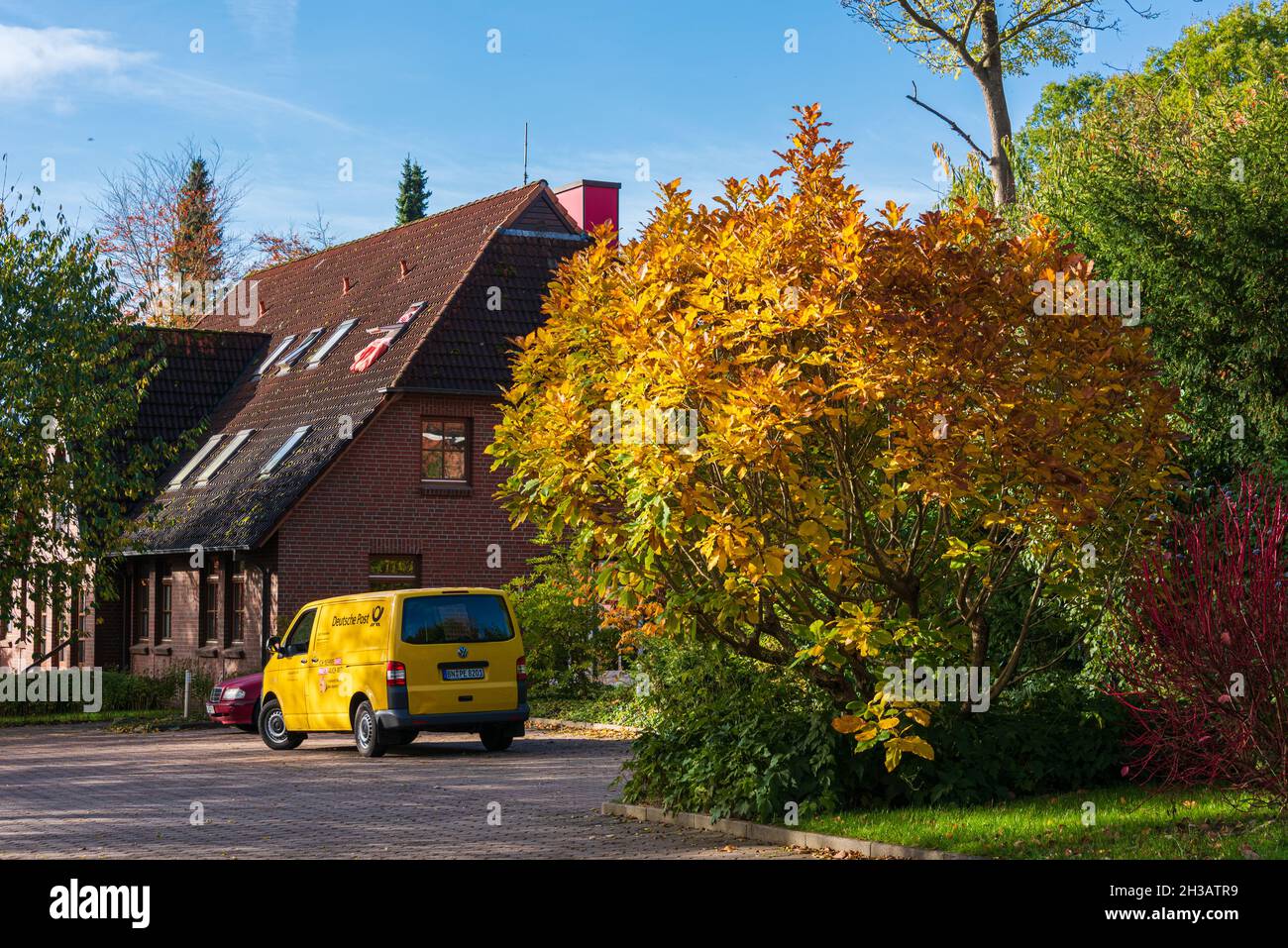 Bunter Herbstlicher Busch und Lieferfahrzeug der Deutschen Post in gleicher Farbe Stock Photo