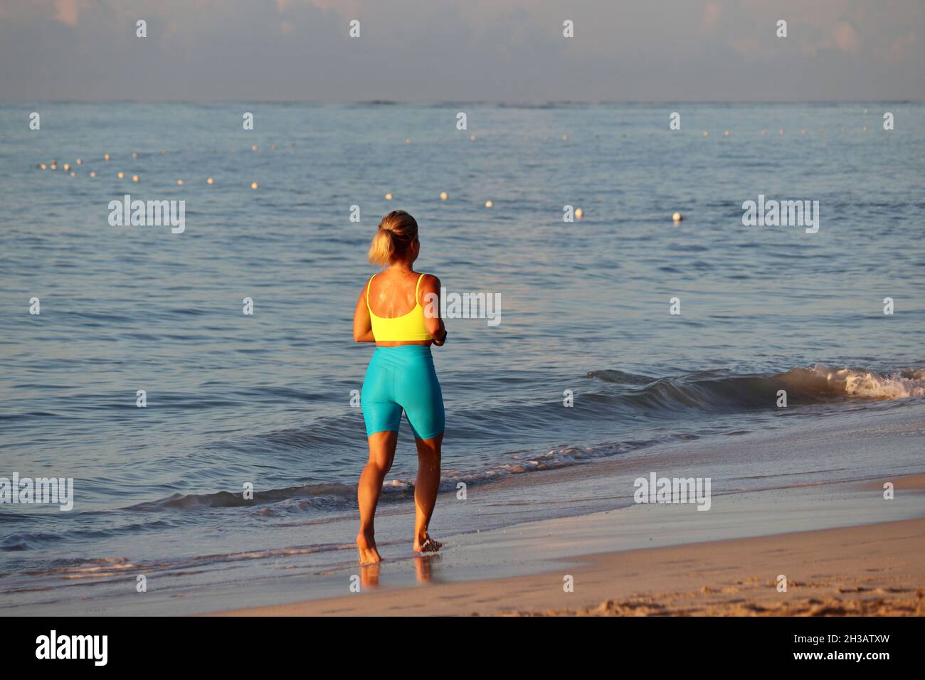 Barefoot woman in sportswear running by the sand in the sea waves. Workout on a beach at early morning, healthy lifestyle Stock Photo