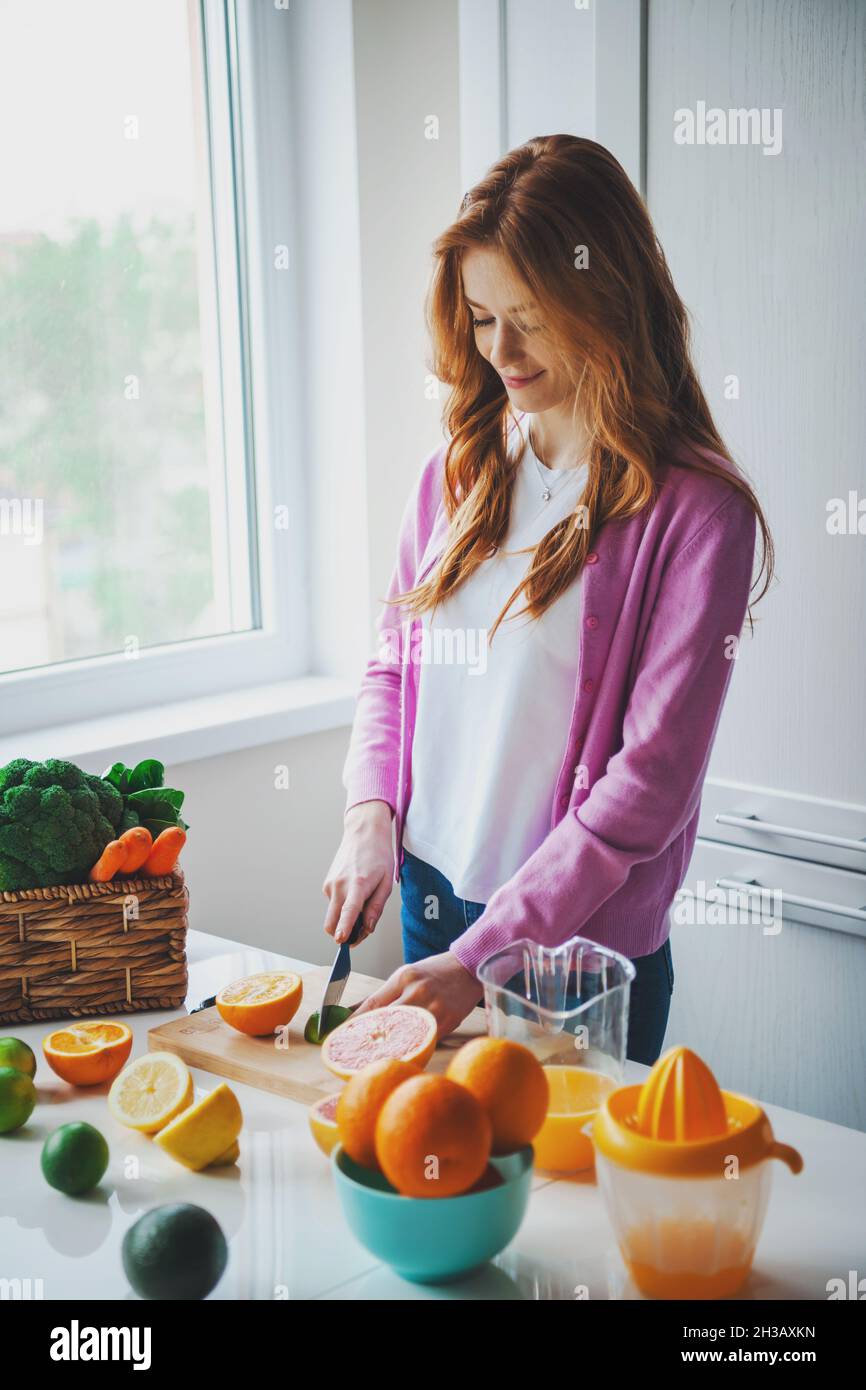 Red-haired woman cuts the ingredients needed for a healthy citrus juice in the kitchen. Healthy lifestyle. Stock Photo