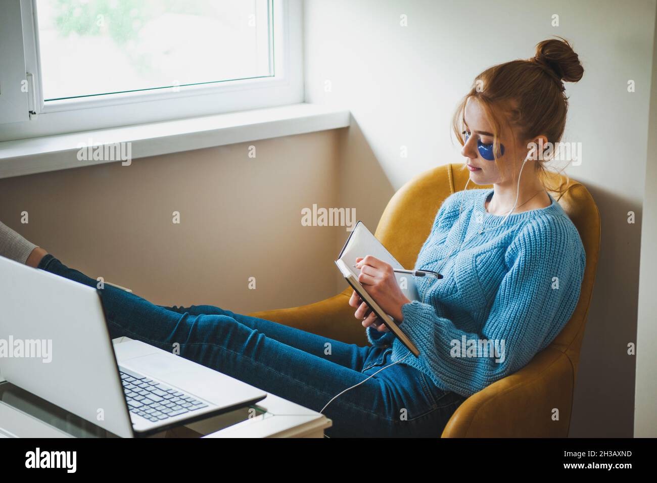 Woman taking notes while participates at online classes sitting relaxed on armchair. Freelance work. Stock Photo