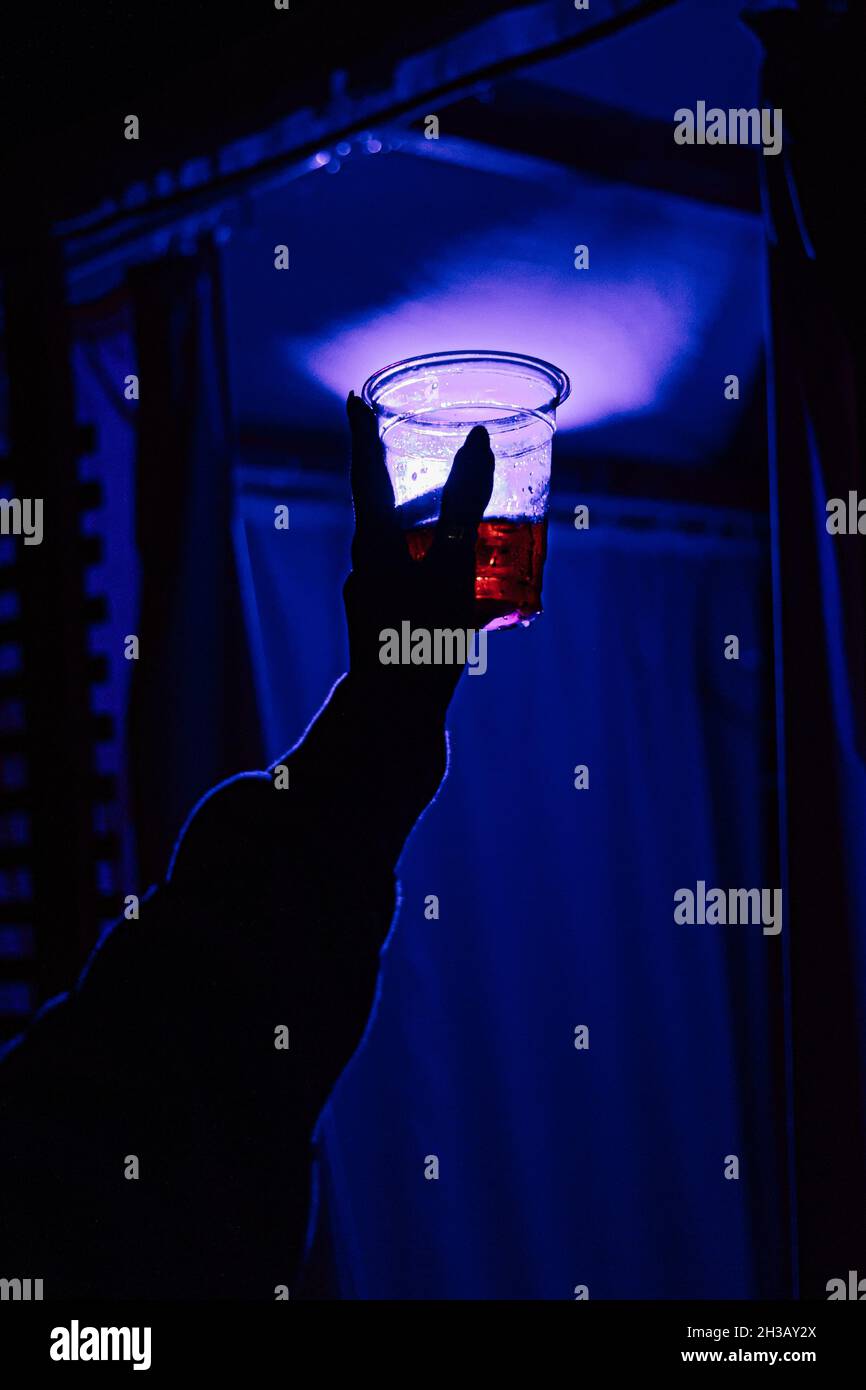 Female hand holding her cocktail cup up to the air in a blue illuminated room while partying