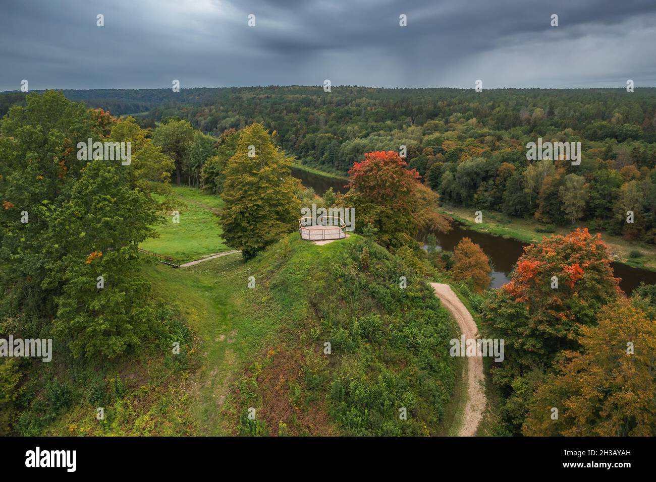 Punia mound in Lithuania with green grass and autumn trees background, road to mountain Stock Photo