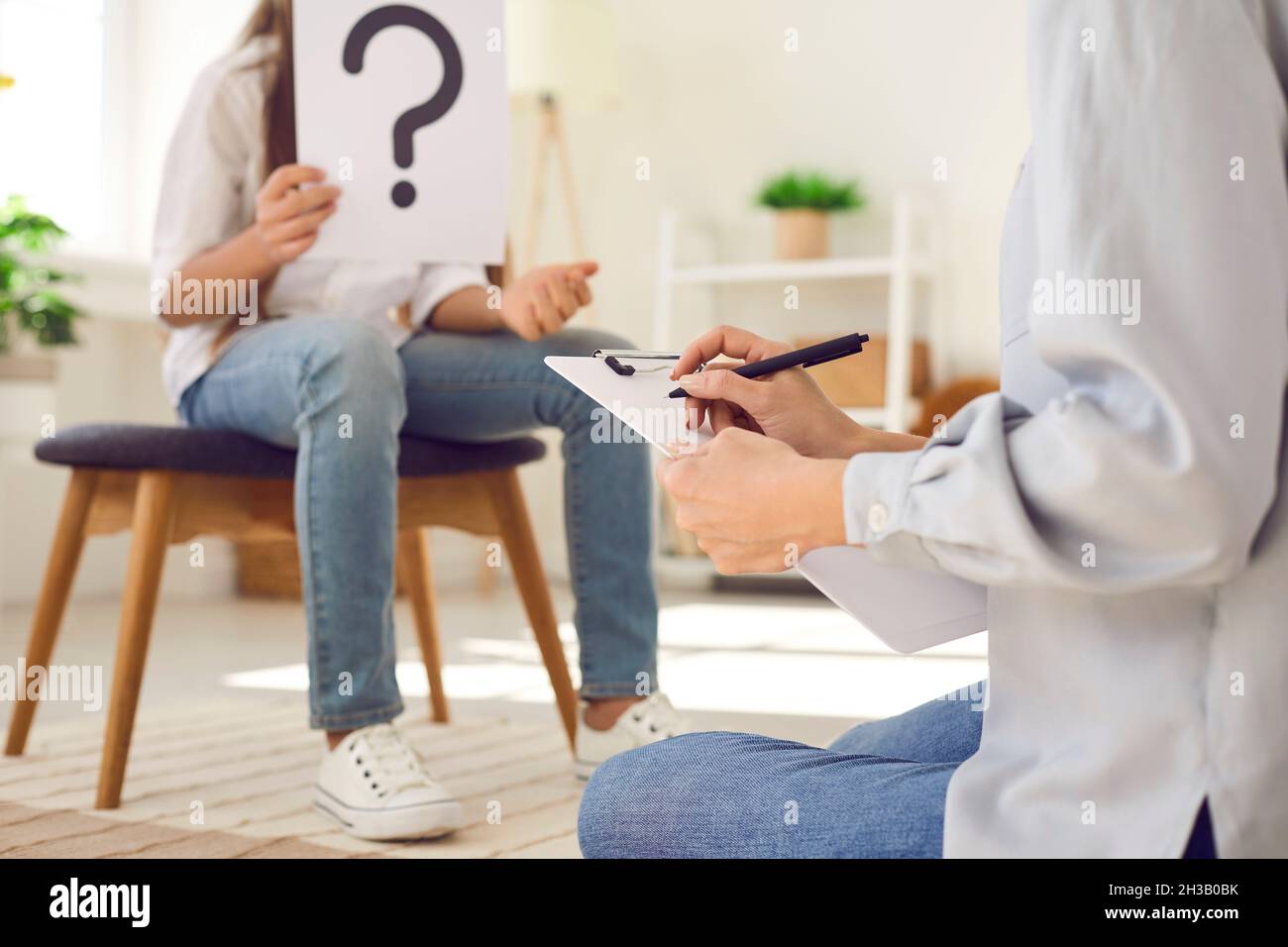 Psychologist or therapist taking notes while interviewing child during therapy session Stock Photo