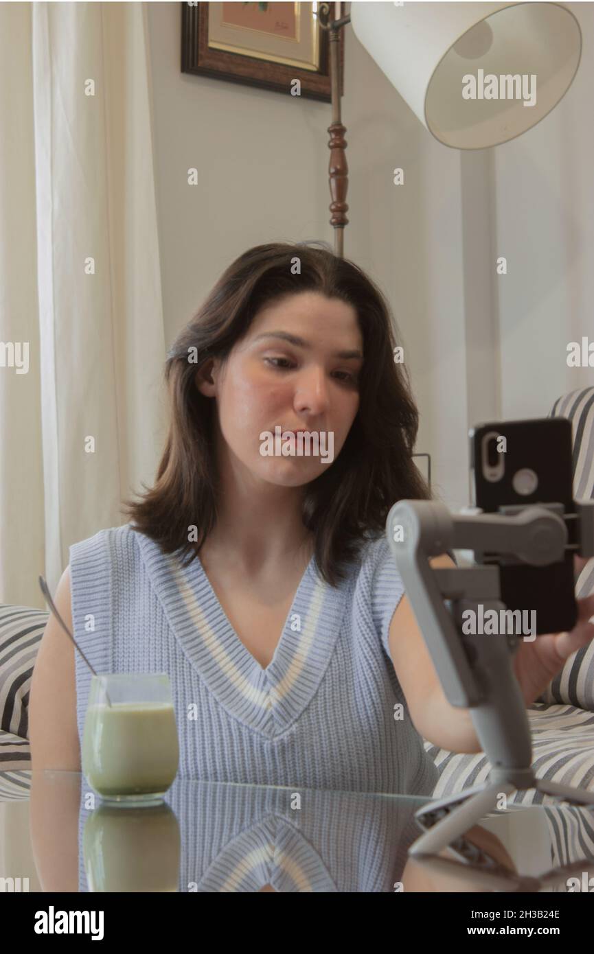A young blogger finalizing live video with her followers for her social media while holding her favorite matcha latte. Wellness concept. Stock Photo