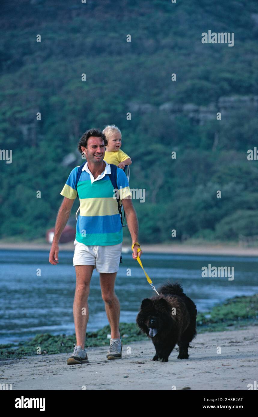 Father and son walking on the beach with their Newfoundland breed dog. Stock Photo