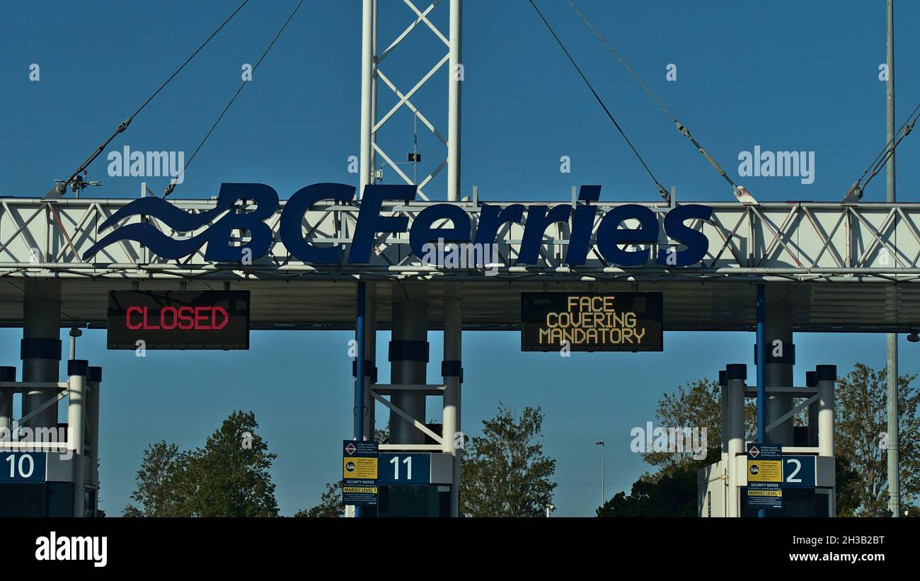 Entrance to BC Ferries Tsawwassen Terminal with blue lettering and information displayed on monitors ('closed' and 'face covering mandatory'). Stock Photo