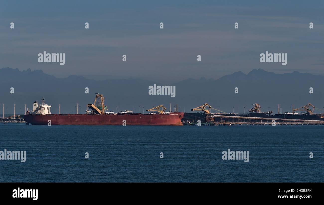 Bulk carrier Hyundai Atlantic loading coal at Roberts Bank Superport, part of Vancouver Harbour with the silhouettes of mountains in background. Stock Photo