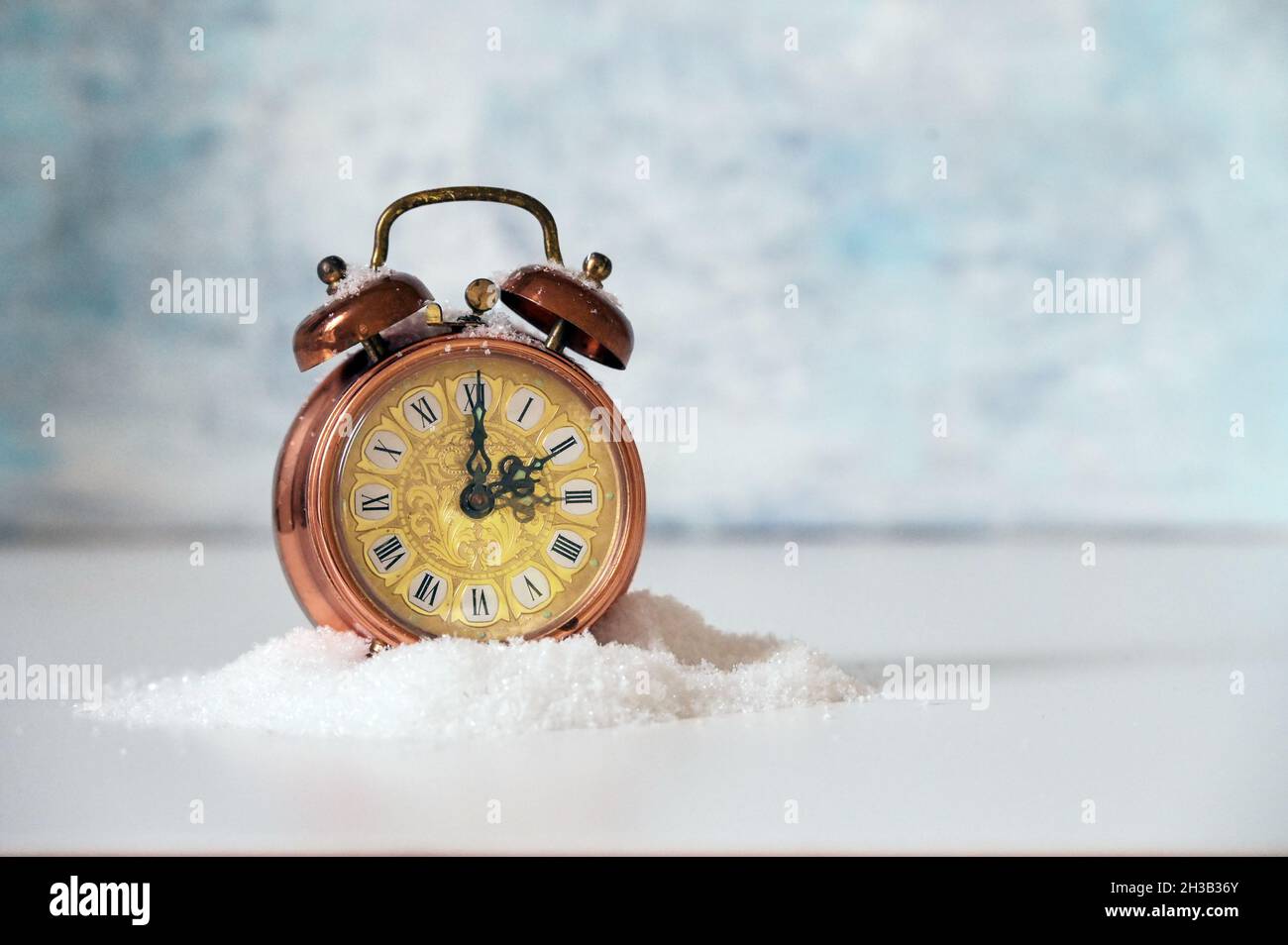 Vintage alarm clock in artificial snow showing clock change to winter time, light blue background with copy space, selected focus, narrow depth of fie Stock Photo