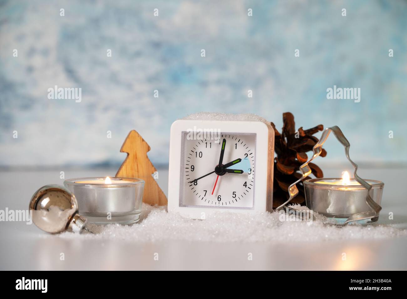 Changing to winter time, modern alarm clock showing the hour switch, artificial snow, candles an Christmas decoration against a light blue background, Stock Photo
