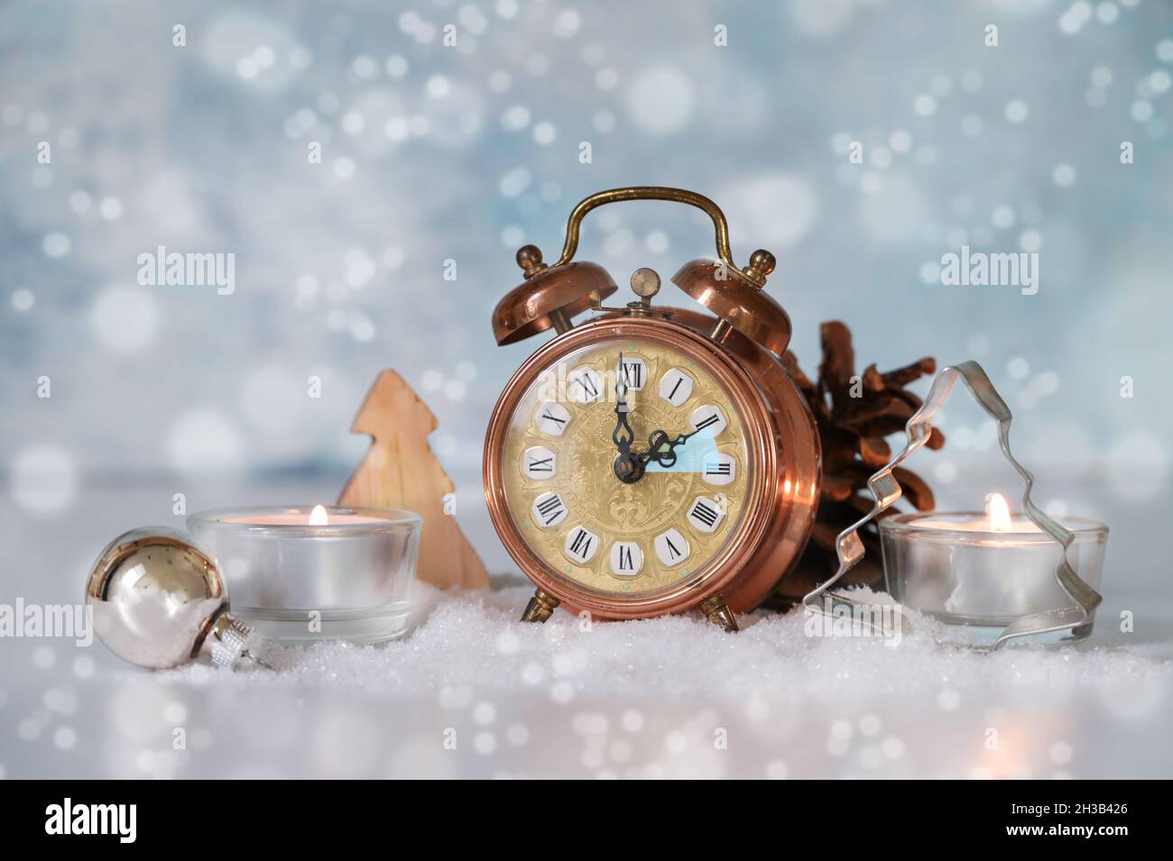 Changing to winter time, vintage alarm clock set back one hour, candles and seasonal decoration against a snowy light blue background, copy space, sel Stock Photo