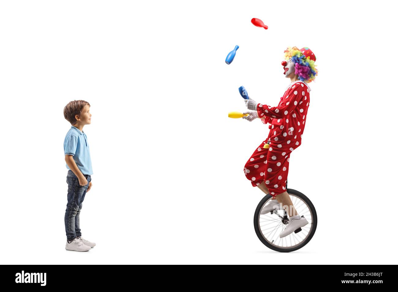 Full length shot of a boy standing and looking at a clown juggling on a ...