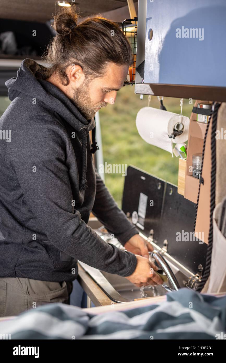 Man washing the dishes inside a caravan Stock Photo