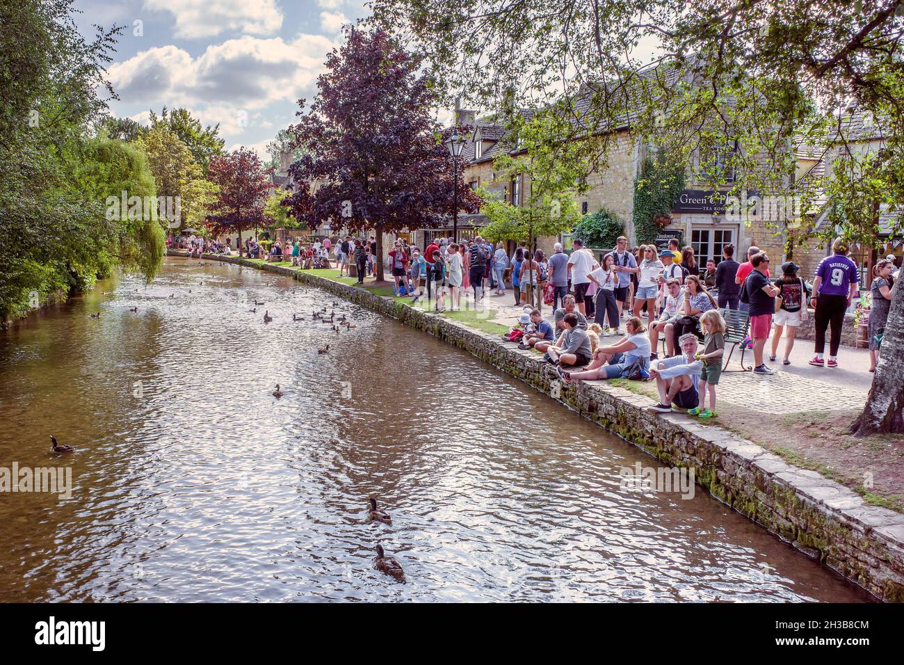 Visitors to Bourton On The Water line the bank of the River Windrush. The Cotswolds, United Kingdom. Stock Photo