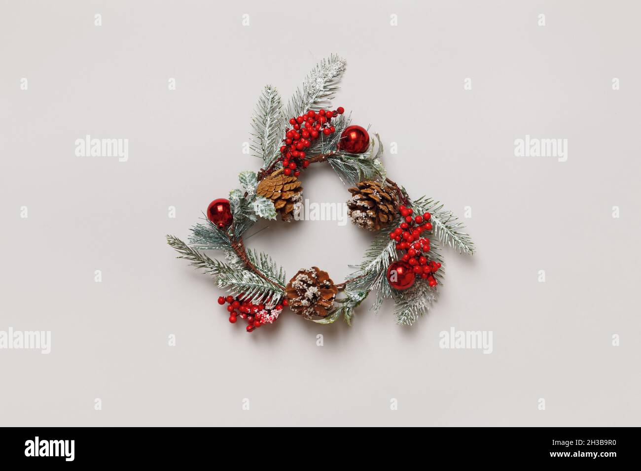 Christmas artificial wreath from branches of evergreen trees with cones and berries on an isolated light gray background. Stock Photo