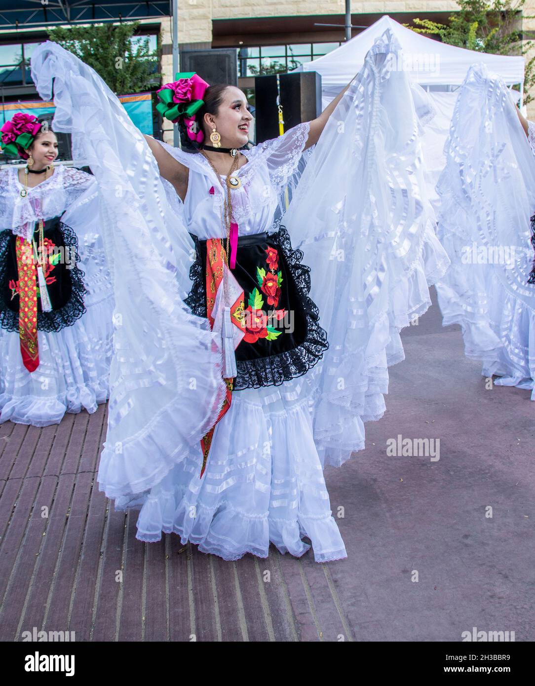 10-09-2021 Tulsa USA -Beautiful young Hispanic dancer holds us the skirts of white lacy skirts of traditional costume while dancing in street.j Stock Photo