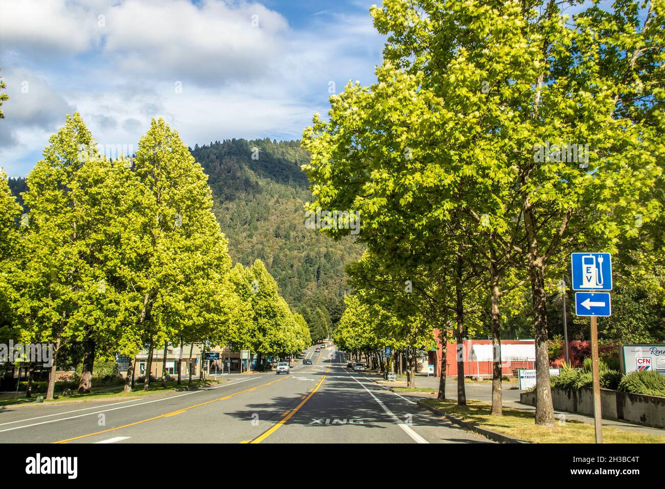 2021 05 27 Willow Creek CA USA - Highway through small Humbolt mountain town in summer with sign for electirc car charge - forested mountain with fire Stock Photo