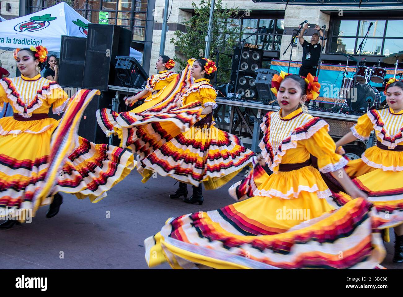 2021 10 09 Tulsa USA Dancing Hispanic girls swirl their beautiful yellow costumes as they dance at a street Festival in front of a stange and speakers Stock Photo