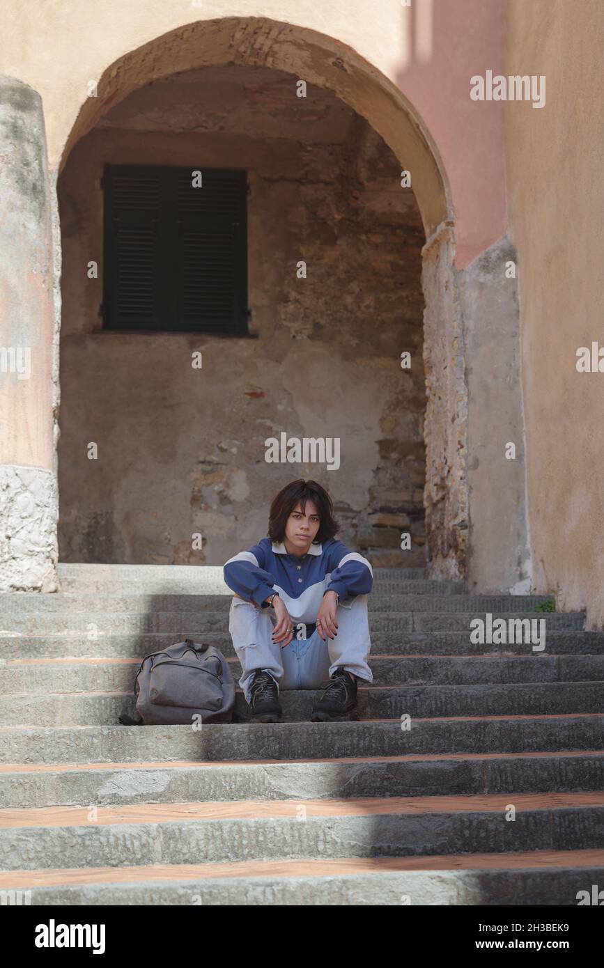 Teenage student with backpack sitting on steps in the street of the Italian old town Stock Photo