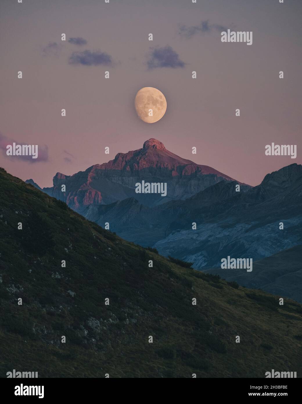 Moon rising during sunset aligned with mountain peak top, Pyrenees. Stock Photo