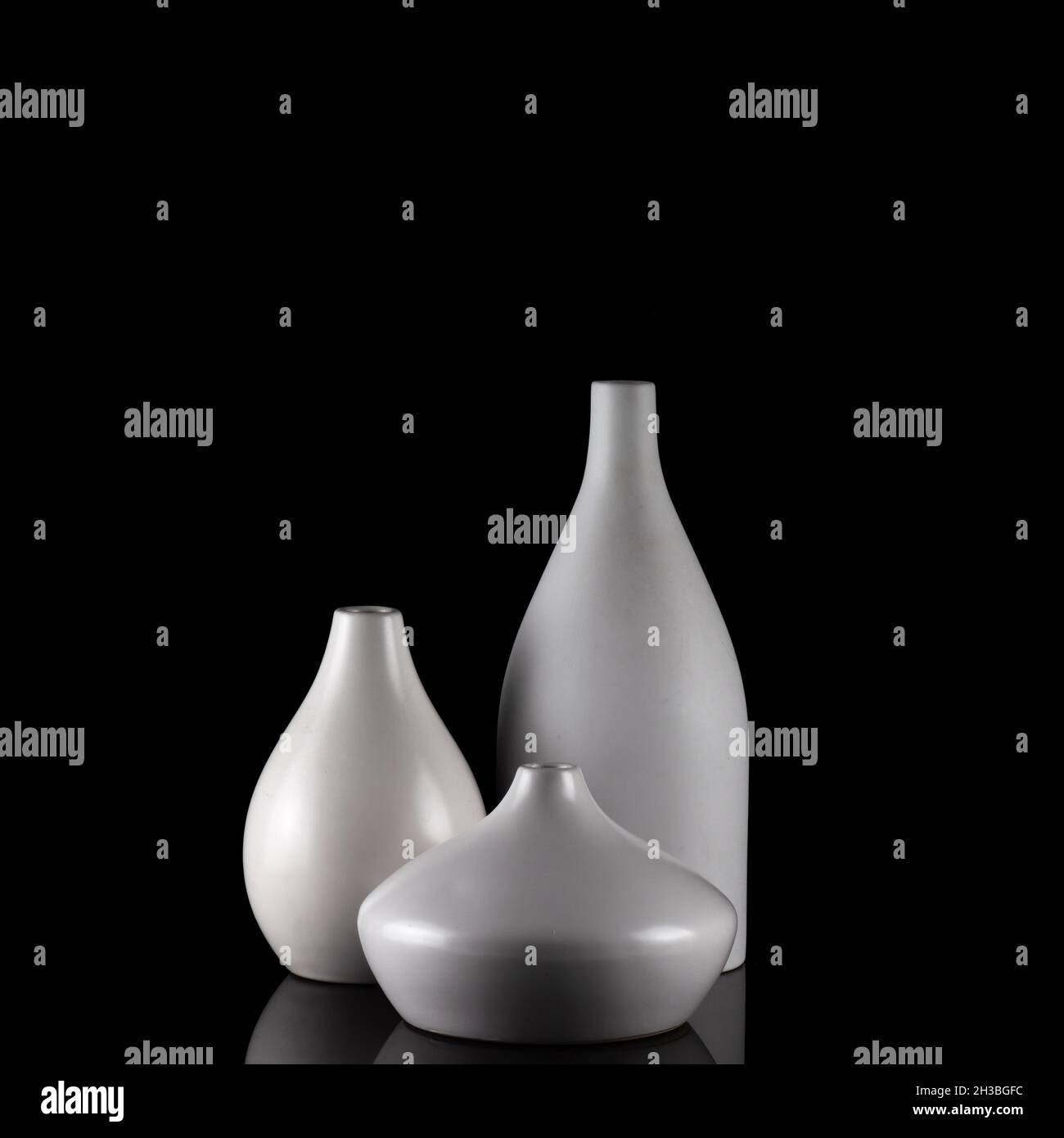 Three curvy white vases on black, with reflection. Stock Photo