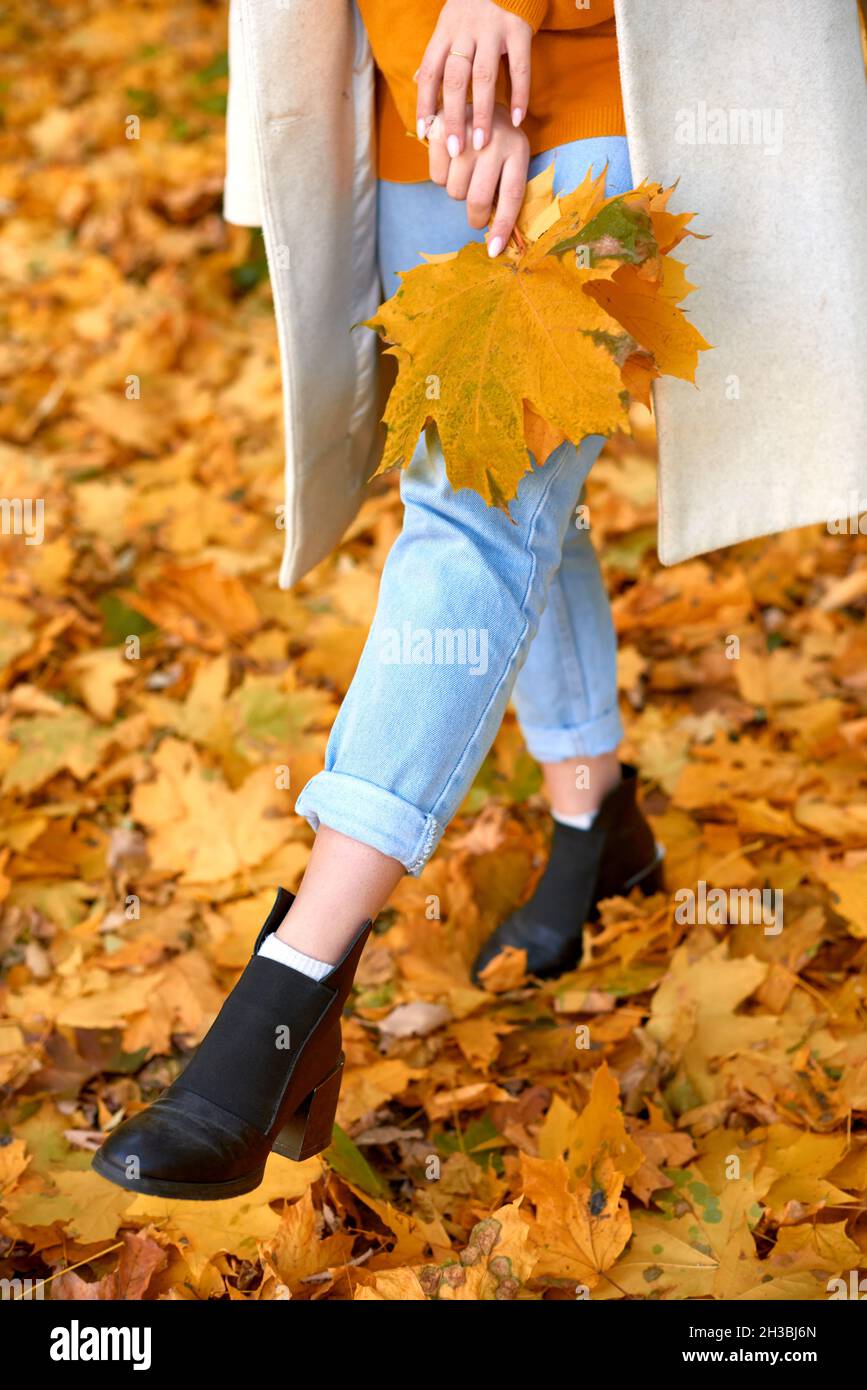 woman holding a bouquet of leaves and kicks leaves by foot in park. shallow depth of field vertical photo Stock Photo